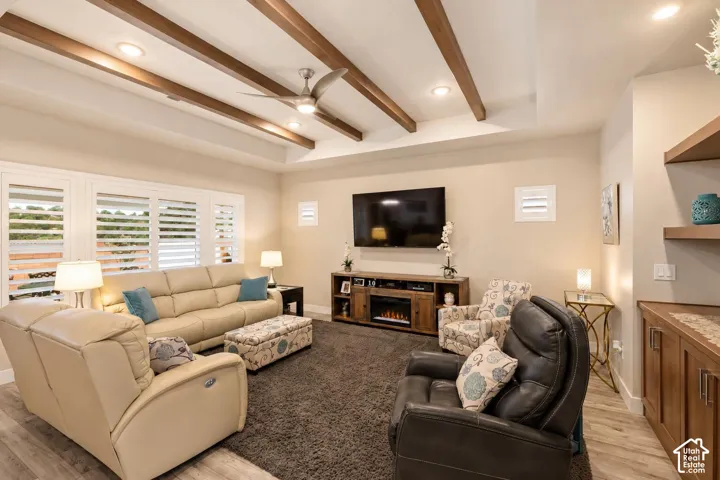 Living area featuring a tray ceiling with exposed wood beams, recessed lighting, wood-finish flooring, plantation shutters, and built-in shelving