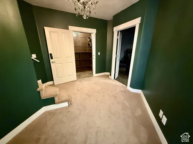 Room featuring wall-to-wall carpeting, crystal chandelier, and two doorways, including a walk-in storage area with built-in wooden shelving and wine rack
