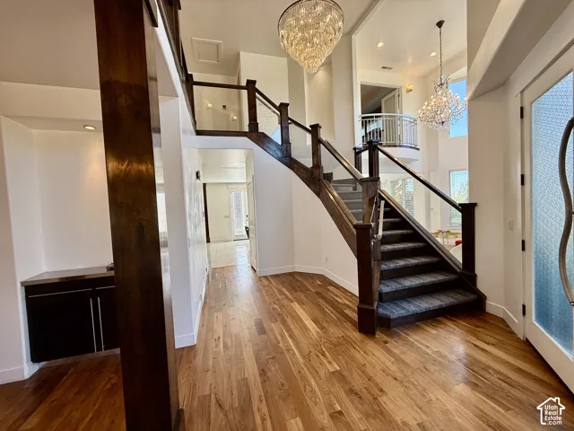 Grand foyer featuring wood-finish flooring, a staircase with custom dark wood railings, dual crystal chandelier fixtures, and a built-in wet bar with dark cabinetry