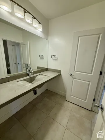 Floating vanity with a concrete-finish countertop and integrated sink basin, chrome-finish faucet, wall-spanning mirror, four-light vanity fixture, and tiled flooring