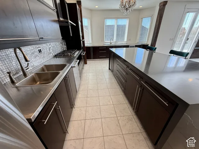 Kitchen featuring dark wood-finish cabinetry, a large central island with solid-surface countertop, mosaic tile backsplash, double-basin stainless steel sink, and marble tile flooring