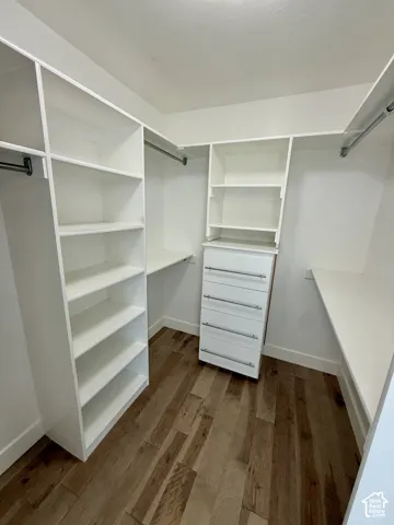 1st Walk-in closet featuring white custom built-in shelving, a built-in dresser with metallic hardware, integrated hanging rods, and wood-finish flooring