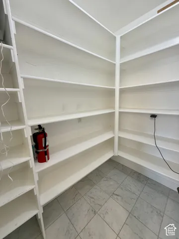 Walk-in pantry area featuring floor-to-ceiling white shelving and marble flooring