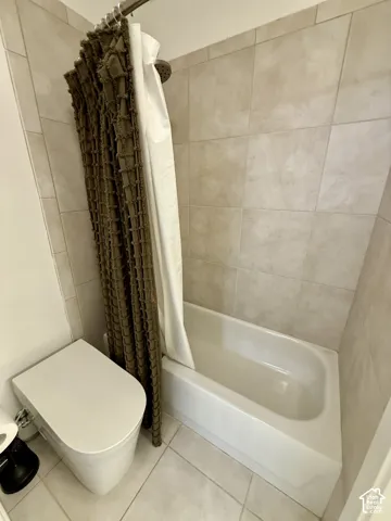Bathtub with shower combination featuring full-height neutral ceramic wall tiling and large-format floor tile