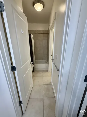 Bathroom featuring neutral ceramic floor tiling, tub surround with integrated shower, and a flush-mount dome light fixture