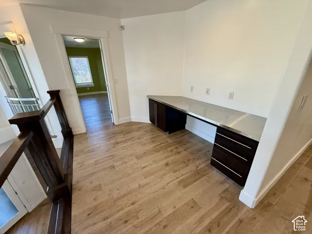 Built-in desk featuring dark-finish cabinetry, a smooth countertop, and wood-finish flooring, accented by a dark wood staircase railing