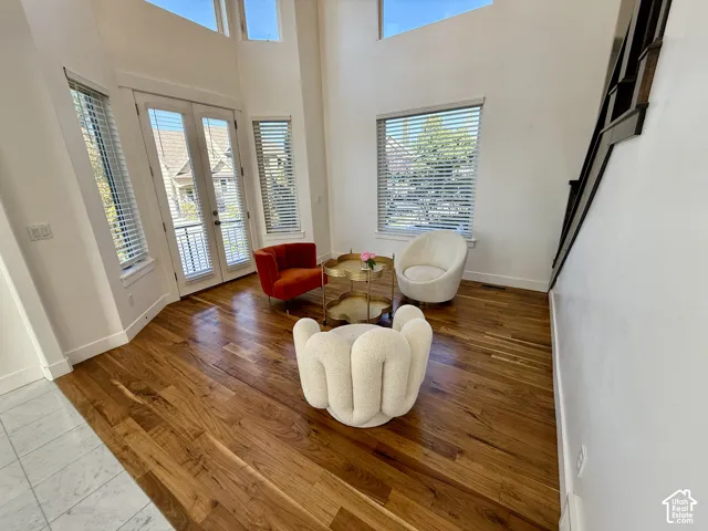 Double-height ceilings featuring expansive windows, wood-finish flooring, glass-paned French doors to Juliet balcony, and a staircase with dark-finished railings