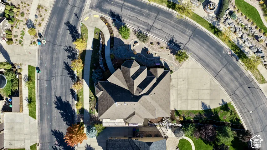 Aerial perspective featuring a multi-faceted roofline, a concrete driveway, and landscaped perimeter grounds situated on a corner lot