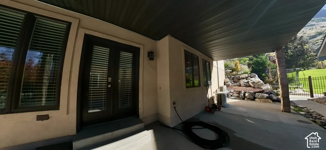 Covered patio featuring a concrete surface, metal soffit, double glass-paneled exterior doors, and exterior wall-mounted lighting