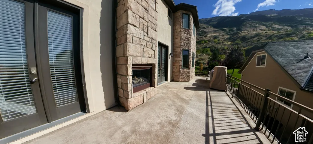 Spacious exterior terrace featuring stacked-stone cladding, a built-in outdoor fireplace, dual French door access, and metal railing overlooking mountains
