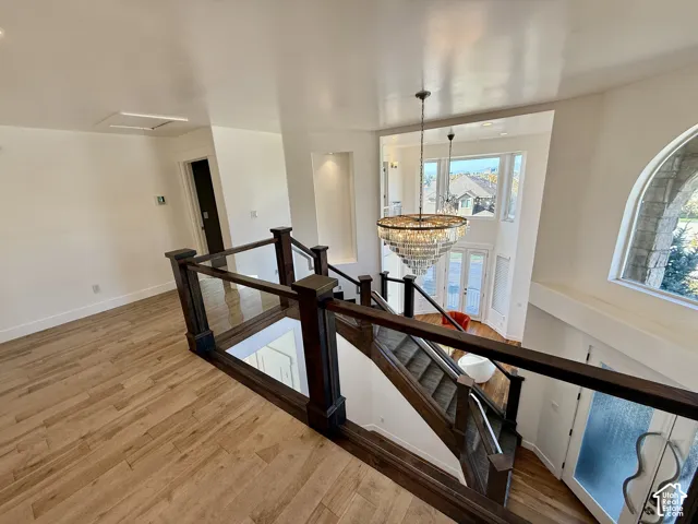 Open landing featuring wood-finish flooring, a tiered crystal chandelier, and a wood railing with glass panels