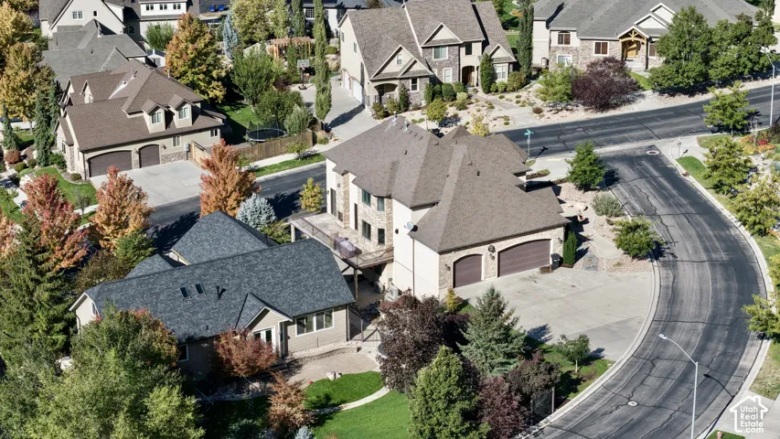 Aerial perspective featuring a multi-level residence with shingled roofing, a paved driveway, an attached garage, and a rear elevated deck