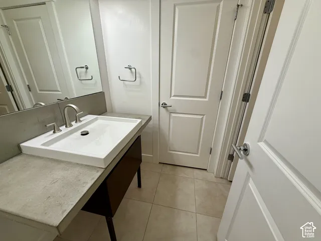 Floating vanity featuring a square vessel sink, stone-surface countertop, metal hardware, and tiled flooring
