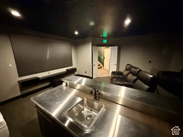 Media room featuring a recessed ceiling with fiber-optic starlight detail, a large wall-mounted projection screen, and a bar island with a metal countertop, undermount sink, and matte black faucet