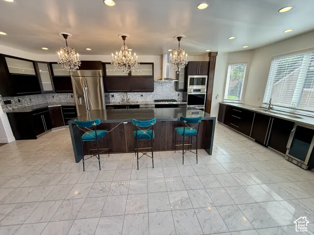 Kitchen featuring dark wood cabinetry, a large center island with a solid surface countertop, stainless steel appliances, a tiled backsplash, and recessed lighting