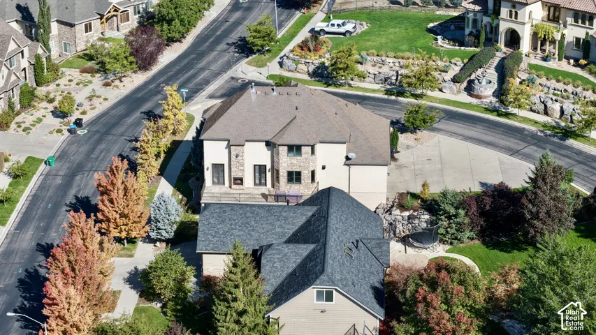 Aerial perspective of a multi-level residence featuring a multi-pitched roof, stone and stucco exterior, stone-clad chimney, and a paved patio area