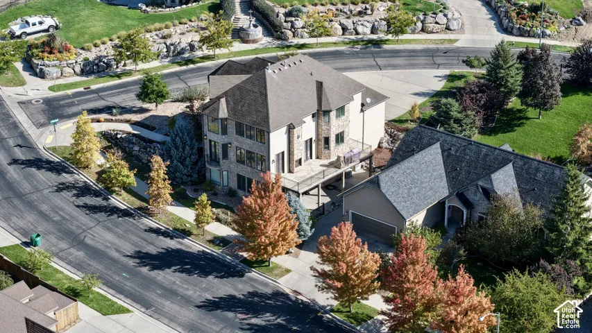 Multi-level residence featuring a stone and siding exterior, expansive elevated deck, multi-pitched roofline, multi-car garage, and tiered landscaping