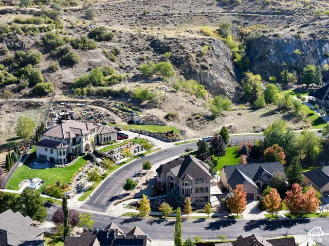 Aerial perspective featuring suburban residential streets, multi-level homes with pitched roofs, mature trees, and prominent hillside topography