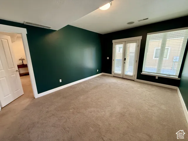 Lower level Den featuring wall-to-wall carpeting, deep-toned accent walls, white-paneled interior door, and glass-paneled French doors with integrated blinds that lead to covered patio