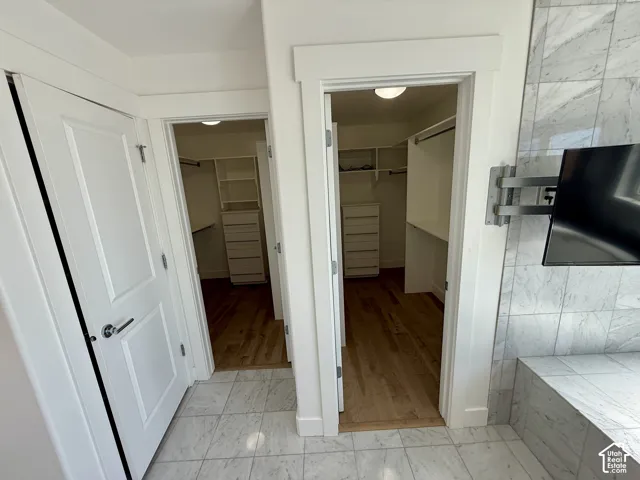 Dual walk-in closets featuring built-in cabinetry, shelving, and wood-finish flooring, complemented by stone-tile flooring and a stone-tiled accent wall