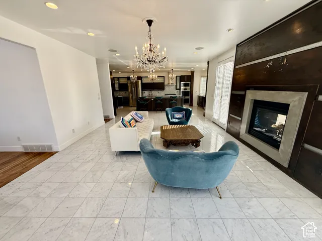 Large-format stone tile flooring, built-in wooden accent wall, recessed fireplace with concrete surround, and dual crystal chandeliers