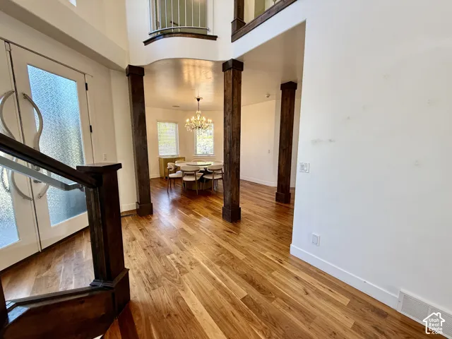 Grand entryway featuring wood-finish flooring, soaring ceilings, stained wood architectural columns, and a multi-tiered crystal chandelier
