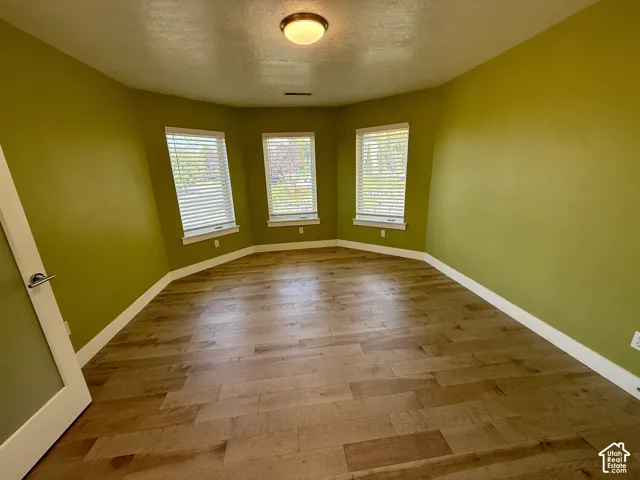 Bedroom 2 featuring wood-finish flooring, a three-panel bay window with integrated blinds, and a flush-mount ceiling light fixture