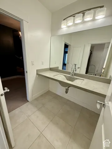 Wall-mounted concrete vanity with an integrated sink, polished chrome faucet, expansive wall-to-wall mirror, four-light brushed metal vanity fixture, and large-format tile flooring