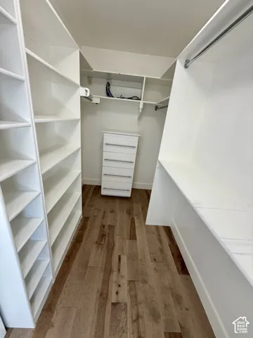 2nd Walk-in closet featuring white built-in shelving, integrated dresser drawers, metal hanging rods, and wood-finish flooring