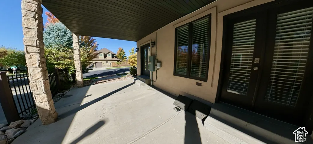 Covered concrete patio featuring stone-clad support pillars and glass-paned double doors from lower level Den
