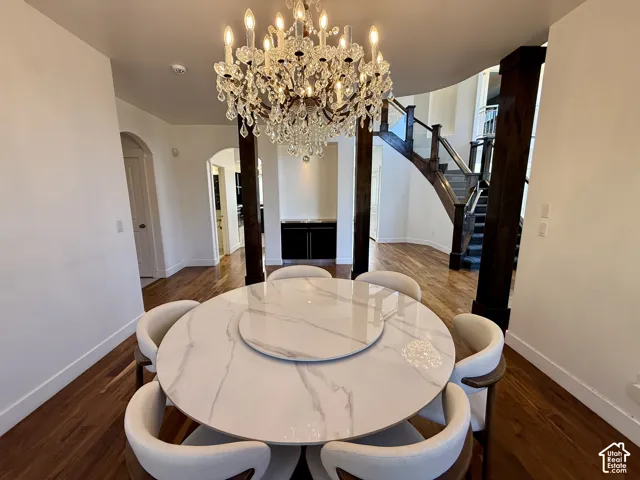 Fomral dinning next to Grand foyer featuring wood-finish flooring, a tiered crystal chandelier, arched doorways, a built-in recessed wet bar with cabinetry, and an open staircase with wood railings