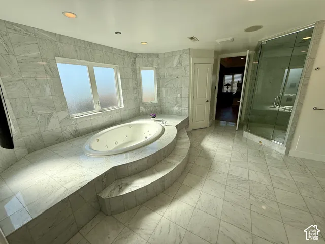 Master bathroomJetted soaking tub set within a raised tile surround, glass-enclosed shower, and floor-to-ceiling stone-tiled walls