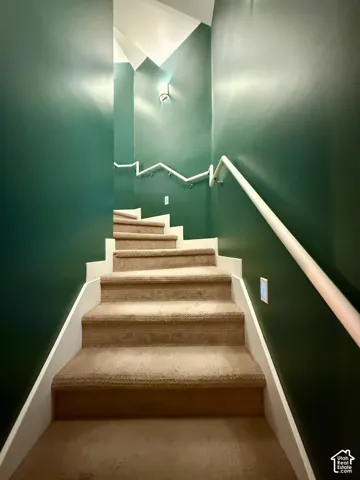Staircase featuring wall-to-wall carpeting, white handrails, and wall-mounted sconce lighting