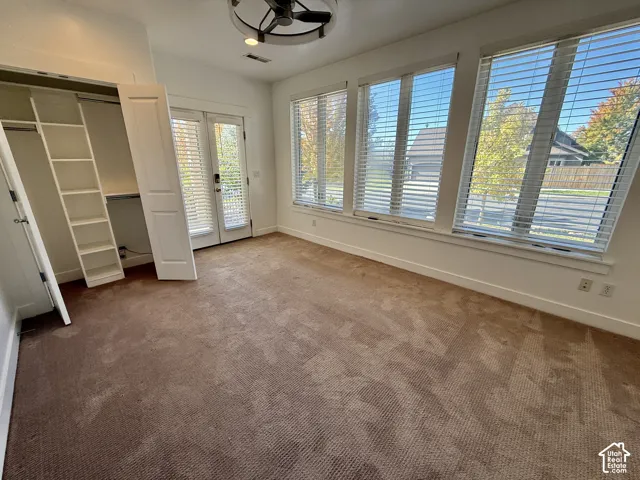 Bedroom 4 featuring oversized windows with integrated blinds, a built-in closet storage system, glass-paneled double doors, and a ceiling-mounted fan with light fixture