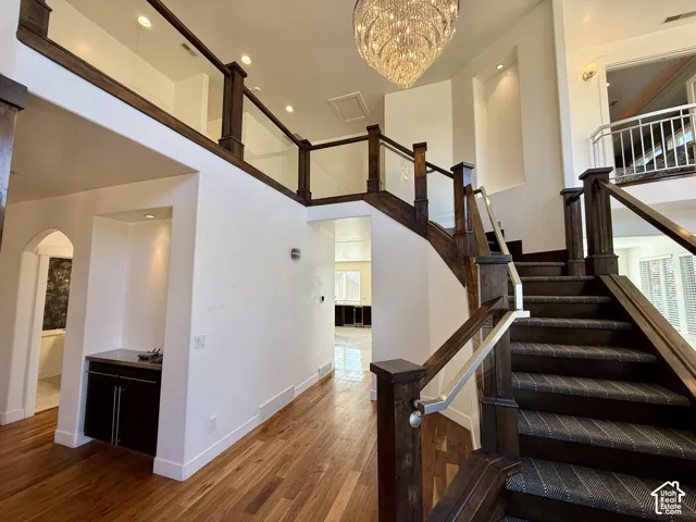 Two-story foyer featuring a grand crystal chandelier, wood-finish flooring, a staircase with custom dark wood railings and glass paneling, and built-in cabinetry with metallic finishes