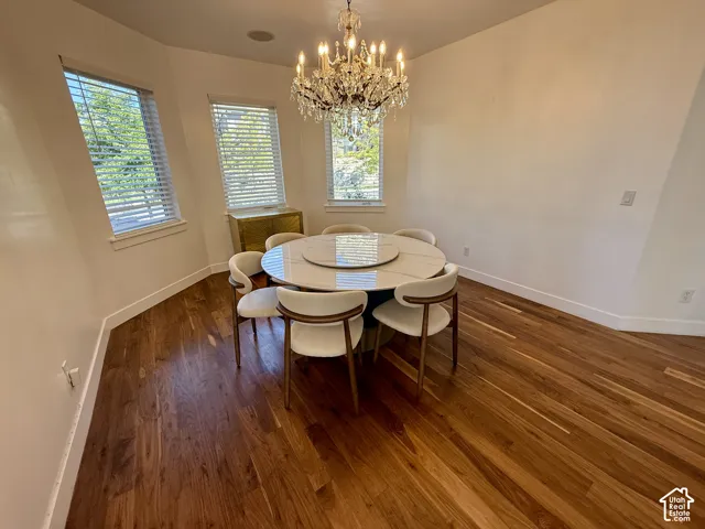 Formal dinning with Bay-style window configuration featuring three windows with horizontal blinds, wood-finish flooring, and a multi-tiered crystal chandelier