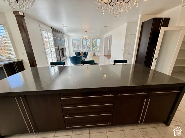 Kitchen featuring a large center island with dark stone-finish countertops, espresso-toned cabinetry with linear hardware, crystal chandeliers, recessed lighting, and marble flooring