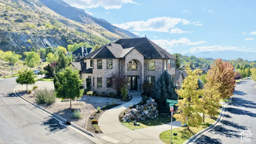 Two-story stone exterior featuring an arched entryway, shingled roof, multi-pane windows, and a paved walkway situated against a mountain backdrop