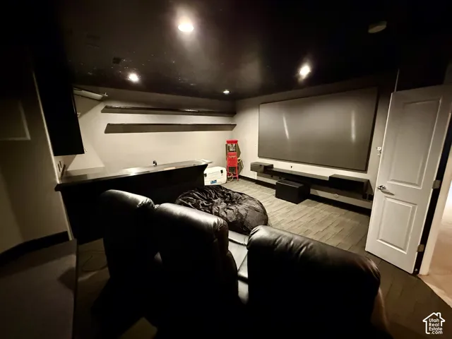 Media room featuring a fixed projection screen, recessed ceiling lighting, built-in bar counter, floating display shelving, and dark-toned flooring