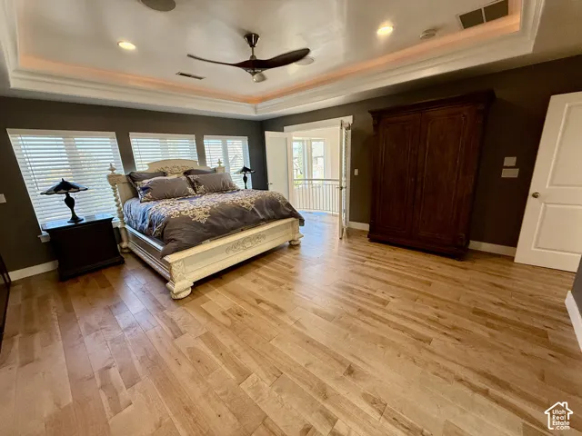 Master bedroom featuring wood-finish flooring, a tray ceiling with recessed lighting, and double-door Juliet Balcony to living room below.