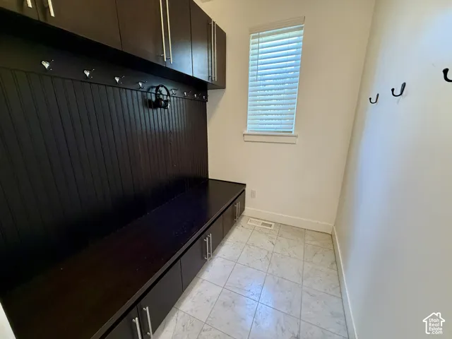 Built-in dark wood cabinetry with beadboard detailing, integrated bench seating, and multiple mounted coat hooks, complemented by marble flooring