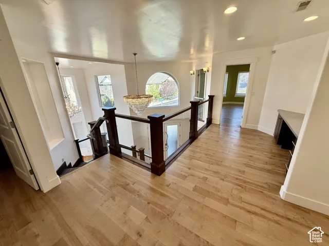 Wood-finish flooring, dark wood railings with glass panels, arched window, multi-tiered crystal chandelier, and built-in desk cabinetry