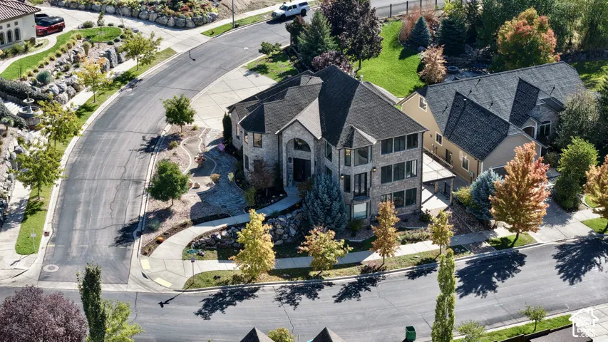 Two-story stone exterior residence featuring a multi-gabled roofline, concrete driveway, stone-accented tiered landscaping, and an attached patio structure