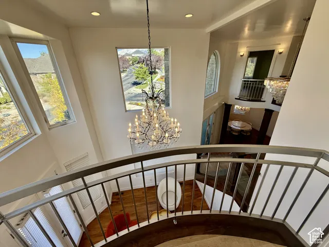 Two-story foyer featuring a curved metal railing and Juliet balcony, multi-tiered crystal chandelier, recessed lighting, expansive multi-pane windows, and wood-finish flooring