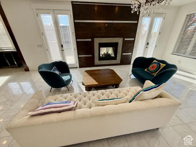 Floor-to-ceiling stone-surround fireplace with wood-paneled accent wall, marbel flooring, two sets of glass-paned double doors leading to a deck and double sided fireplace and a decorative chandelier