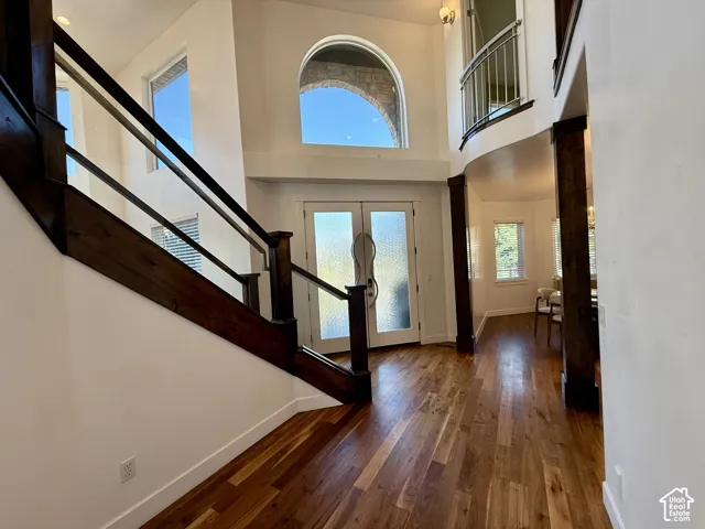 Double-height foyer featuring wood-finish flooring, a grand staircase with dark-stained wood railings, an arched transom window, and a decorative wood-railed interior balcony