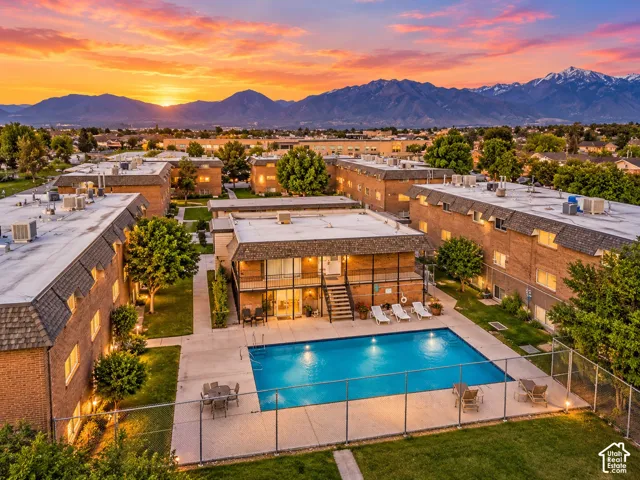 Clubhouse featuring a fenced swimming pool, concrete hardscaping, mature landscaping, and mountain backdrop