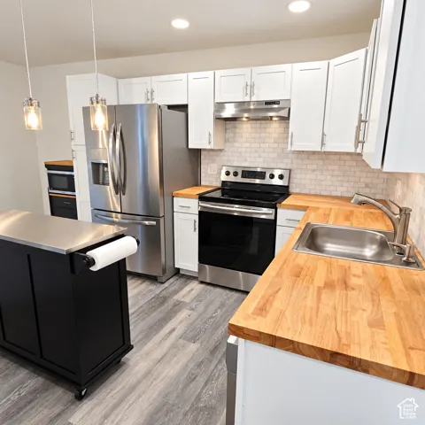Updated Kitchen featuring butcher block countertops, white shaker-style cabinetry, a subway tile backsplash, stainless steel appliances, and a mobile island with a stainless steel surface