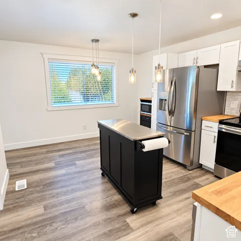 Kitchen featuring white shaker-style cabinetry, butcher block countertops, stainless steel appliances, wood-finish flooring, and glass pendant lighting