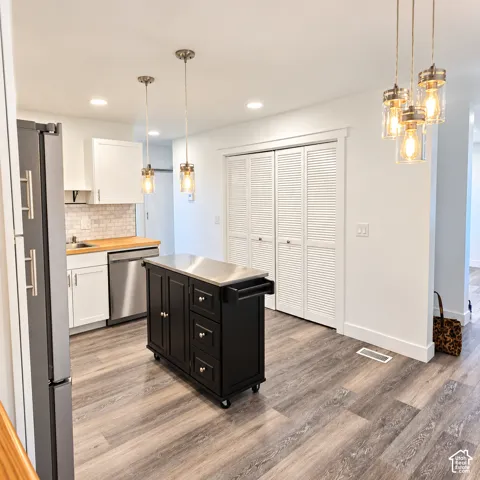 Kitchen featuring wood-finish flooring, white cabinetry with butcher-block countertops, tile backsplash, and decorative glass-shade pendant lighting